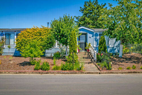 A blue mobile home with bushes in front of it.